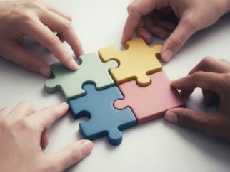 Hands connecting colorful puzzle pieces together.